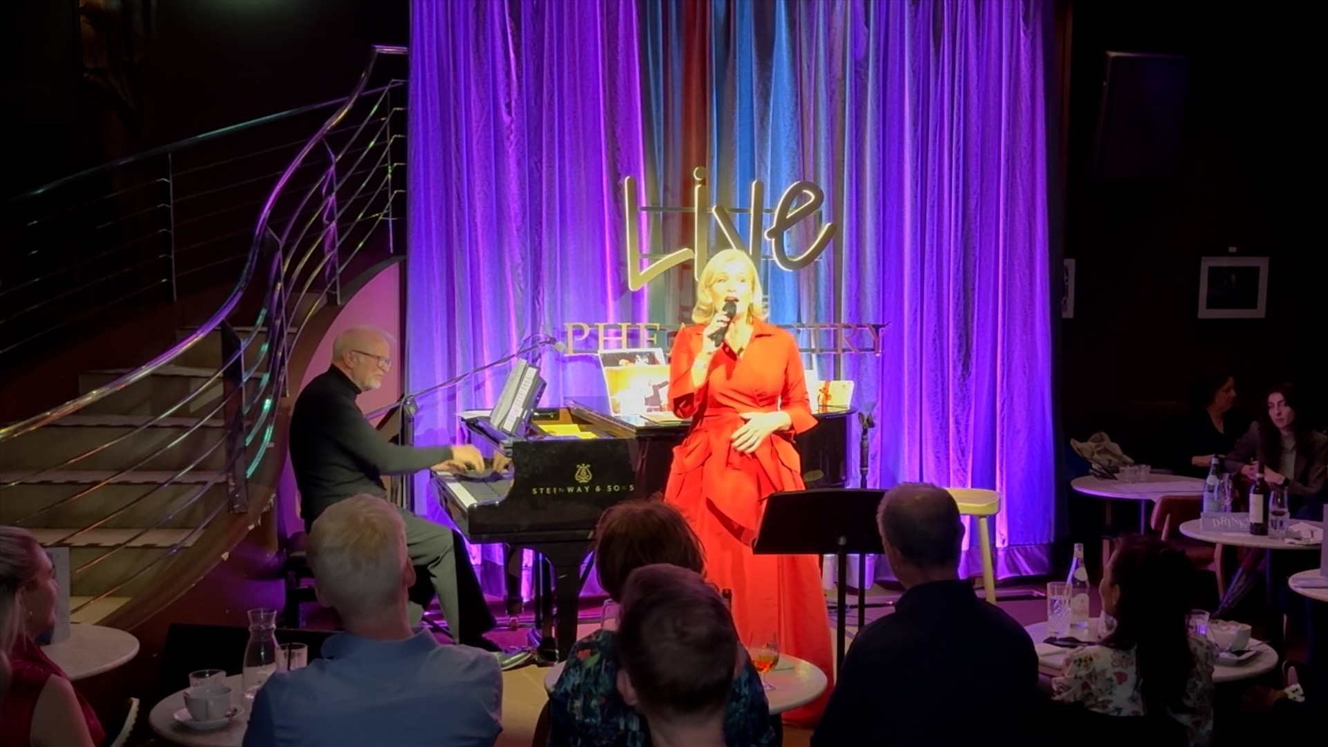 Nicky Gayner in red with Tom Wakeley at the piano during Musical Memories at The Pheasantry